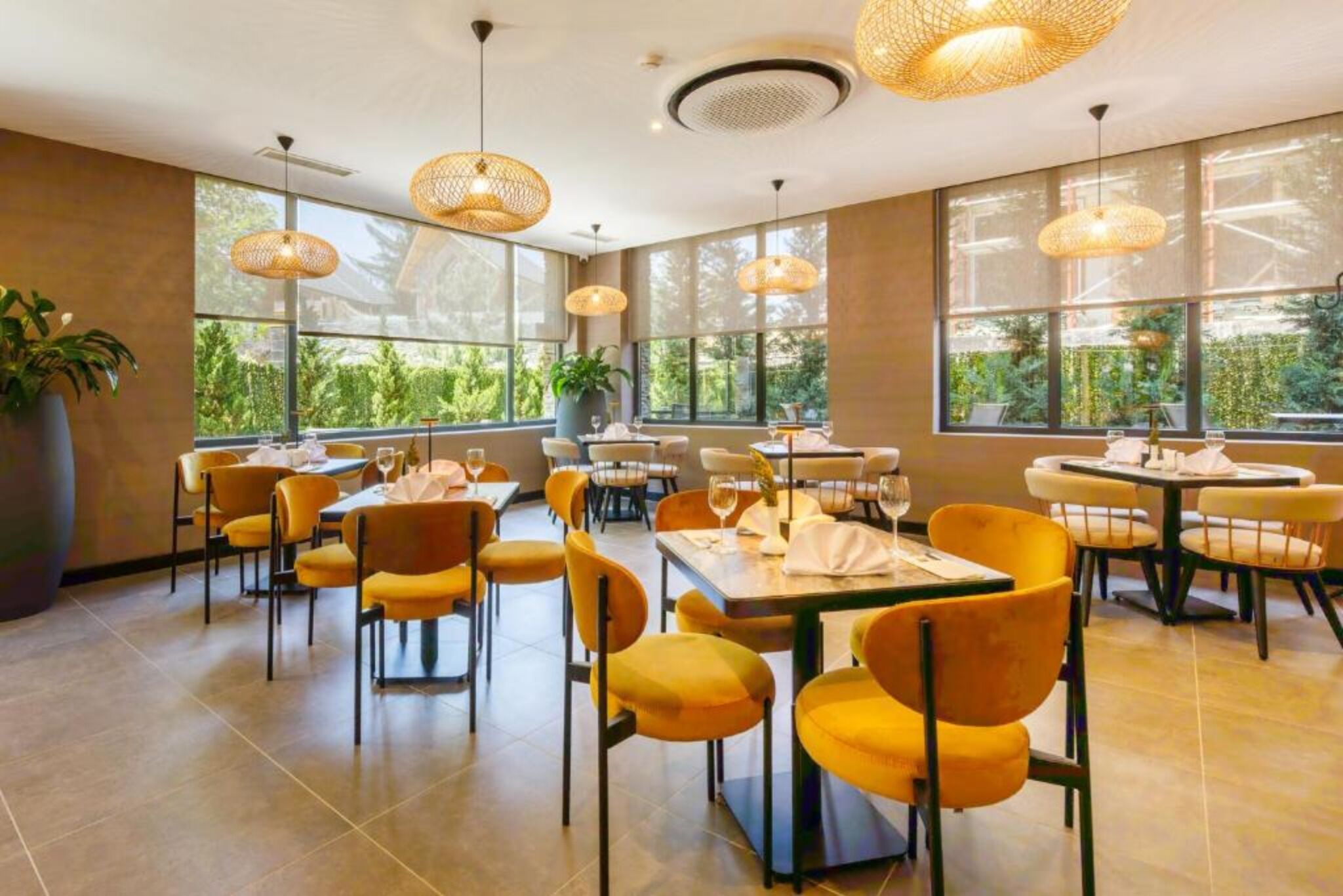 Un restaurante con sillas amarillas, mesas redondas y amplias ventanas con vistas al verdor.