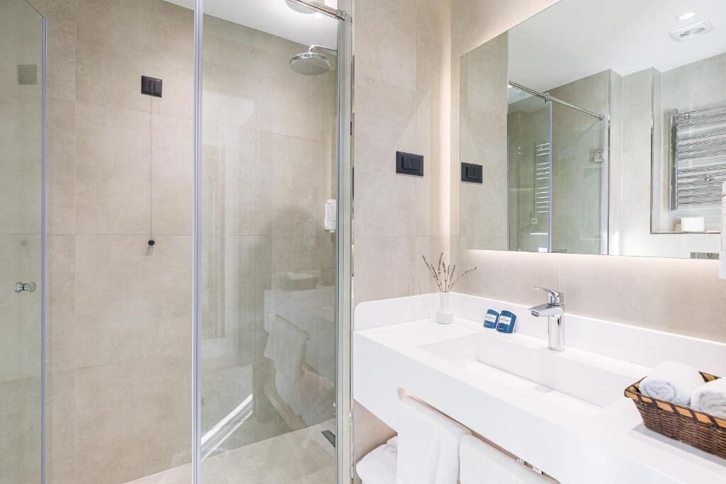 A modern bathroom with a glass-enclosed shower, a white sink with a mirror, and a basket of towels.