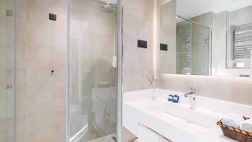 A modern bathroom with a glass-enclosed shower, a white sink with a mirror, and a basket of towels.