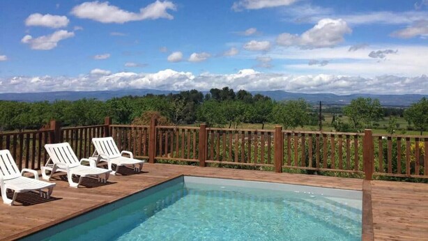A pool area with a wooden deck, white lounge chairs, and a wooden fence.
