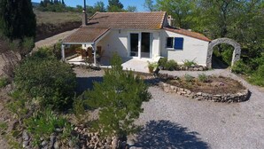 A small, single-story house with a tiled roof, a stone archway, and a patio with outdoor seating.