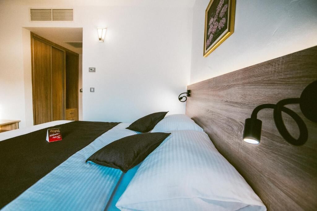 Une chambre d’hôtel avec deux lits, une tête de lit en bois, une lampe de chevet et un panneau d’accueil.