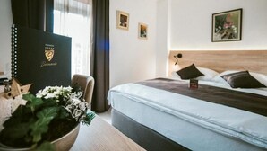 A hotel room with a large bed, a desk with a laptop, a potted plant, and a black folder on the desk.