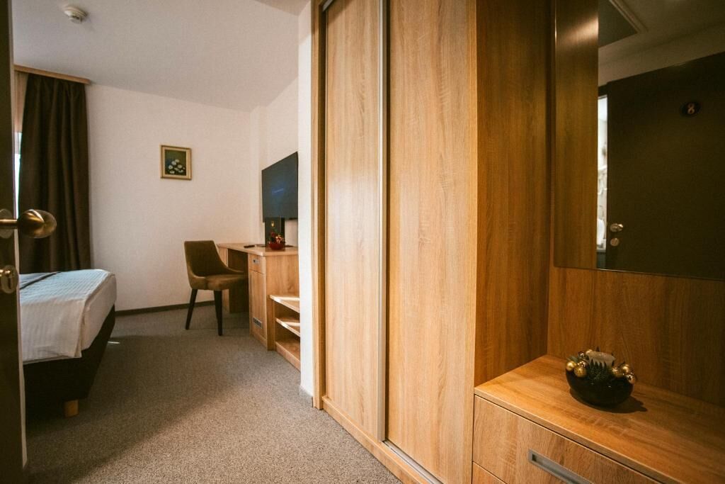 A hotel room with a bed, a desk, a chair, a wardrobe, and a small table with a decorative bowl.