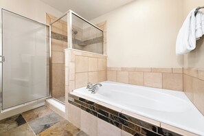 Ein Badezimmer mit einer Glaskabine zur Dusche, einer weißen Badewanne und einem gefliesten Boden.