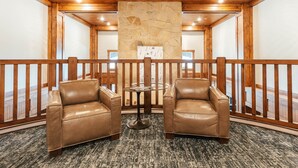 Ein Zimmer mit zwei Ledersesseln, einer Steinwand, einer Holzbalkendecke und einem Balkon mit Holzgeländern.