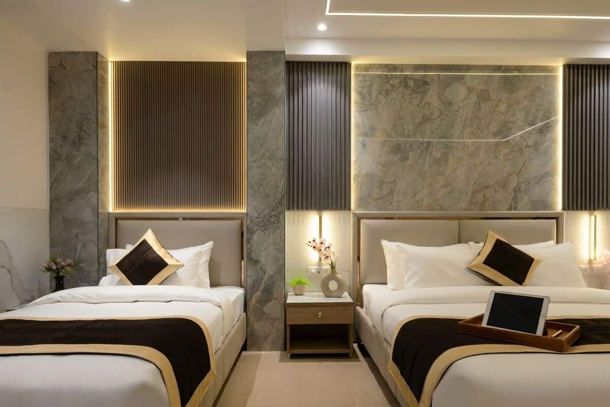 Una habitación de hotel moderna con dos camas, paredes de mármol y mesitas de noche con lámparas.