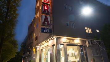A hotel with a prominent neon sign, a visible entrance, and air conditioning units.