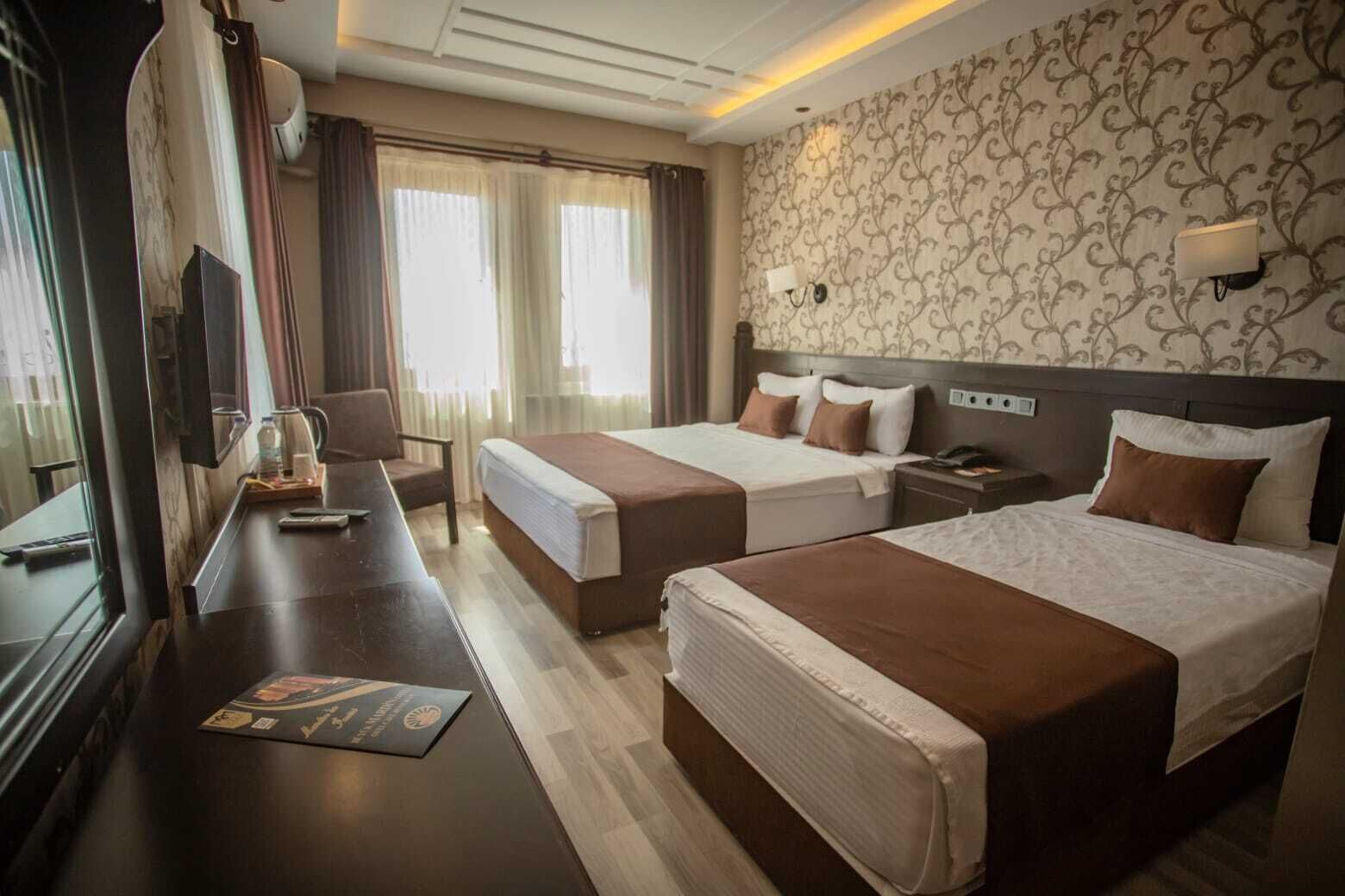 A hotel room with two beds, a desk with a chair, a TV, and a window with curtains.