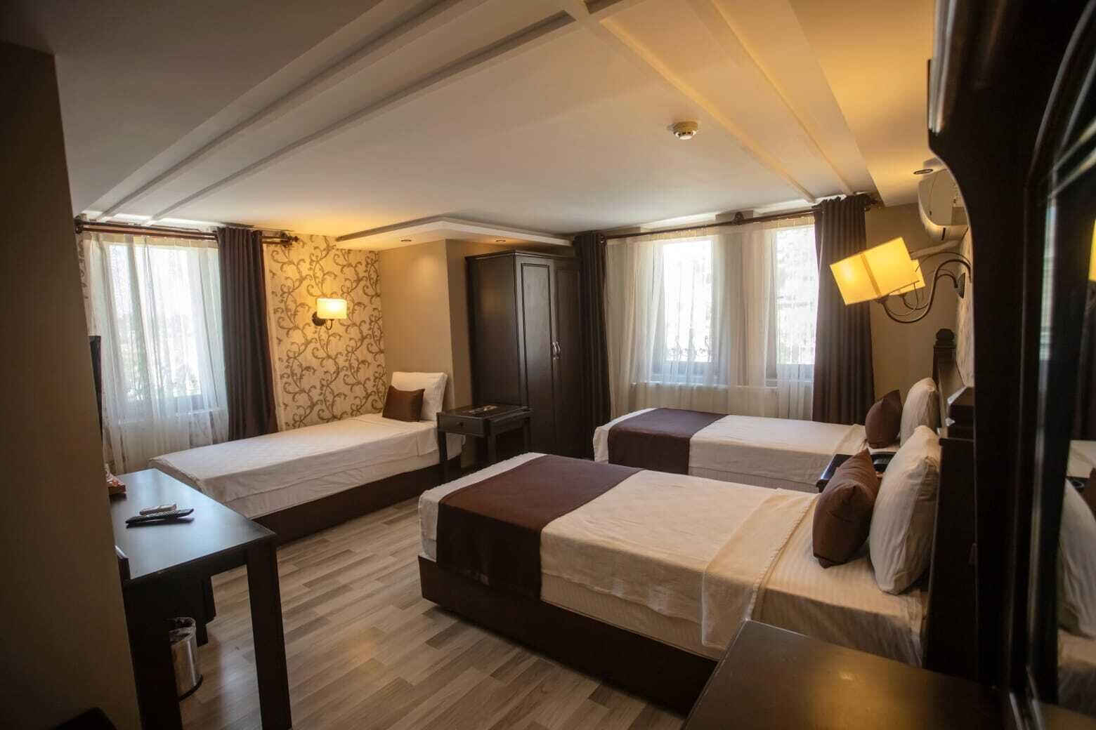 A hotel room with two single beds, a desk, a lamp, and a stone wall.