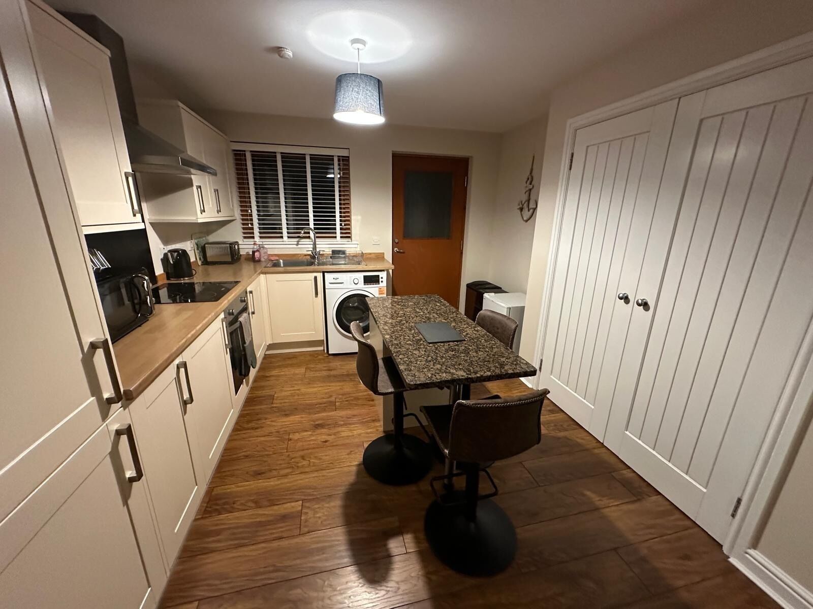 A compact kitchen with wooden flooring, a dining table with chairs, a washing machine, and a sink.