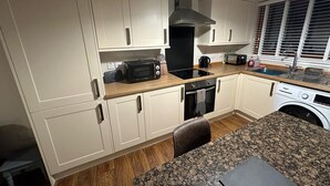 Een compacte keuken met witte kasten, een zwarte magnetron, een fornuis en een wasmachine.