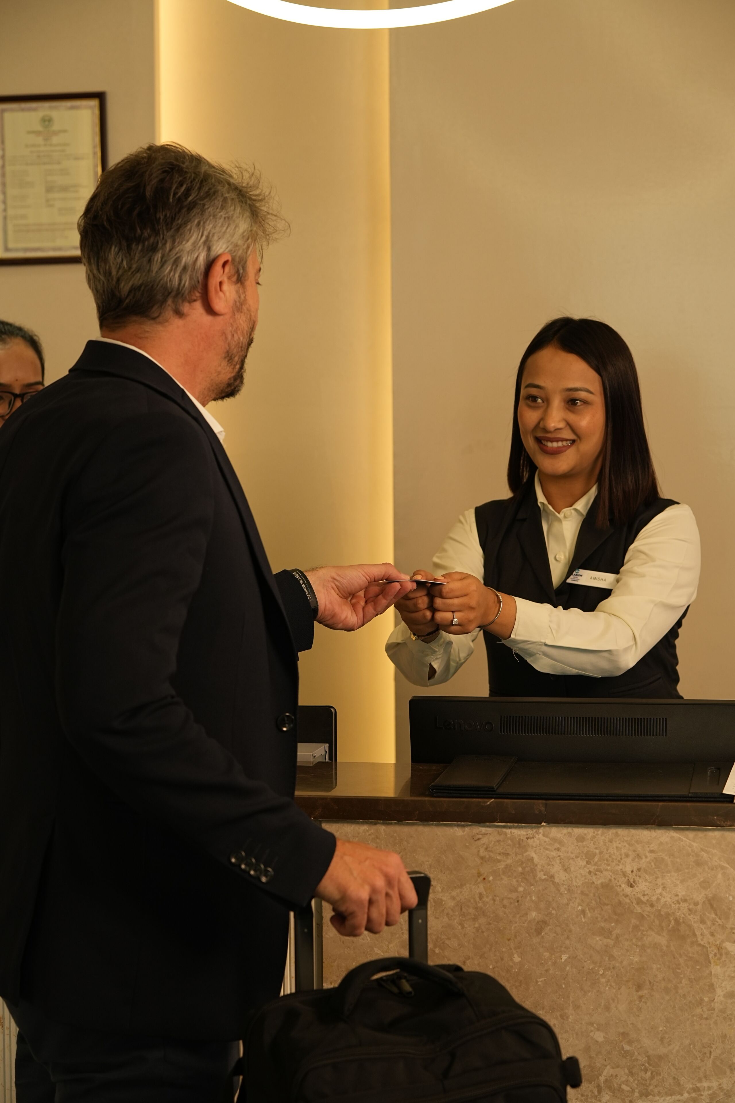 A hotel reception area with a reception desk, a guest with a suitcase, and a staff member handing over a card.