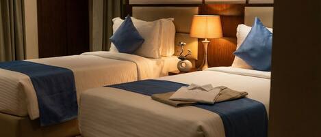A hotel room with two beds, a nightstand with a lamp, and a wall-mounted artwork.
