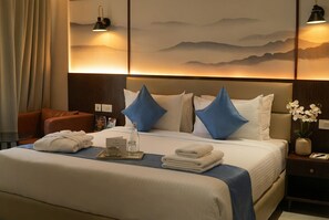 A hotel room with a bed, pillows, a nightstand, a vase with flowers, and a wall with a mountain painting. - Clarion Hotel Hyderabad (Hyderabad)