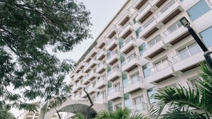 Een hotel met meerdere verdiepingen, balkons, een overdekte doorgang en omliggend groen.