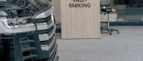 Une zone de stationnement avec voiturier, agrémentée d’un panneau, d’une voiture et d’une personne assise derrière un bureau.