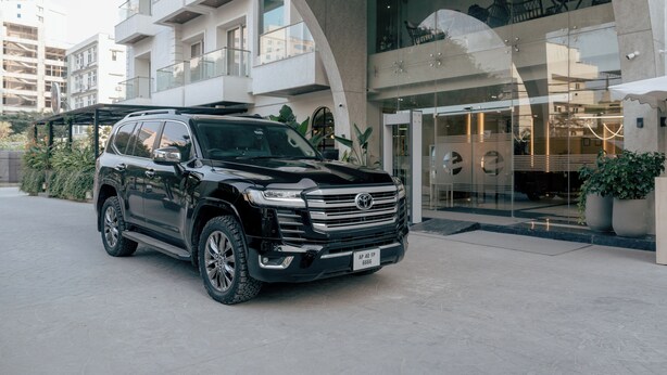 Een zwarte SUV geparkeerd voor een modern gebouw met een glazen ingang en een balkon.