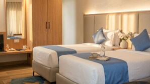 Een hotelkamer met twee bedden, een houten garderobe, een bureau met stoel, een spiegel en een nachtkastje met een bloevas.