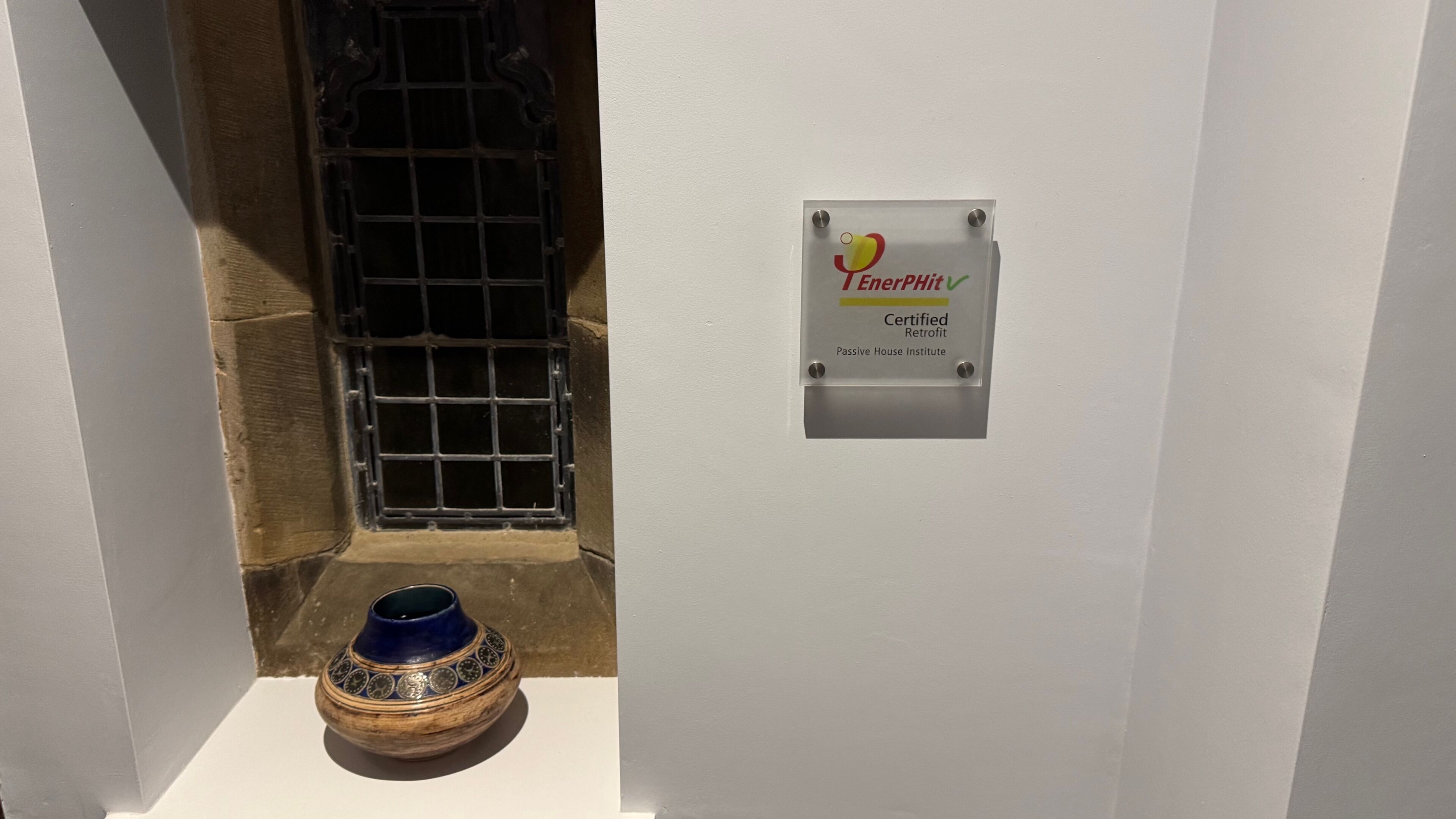 A bathroom with a white wall, a metal door, and a decorative blue vase on the floor.
