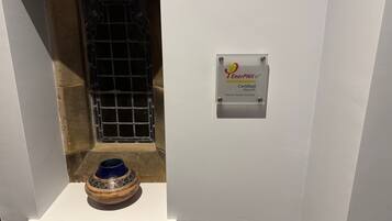 A bathroom with a white wall, a metal door, and a decorative blue vase on the floor.
