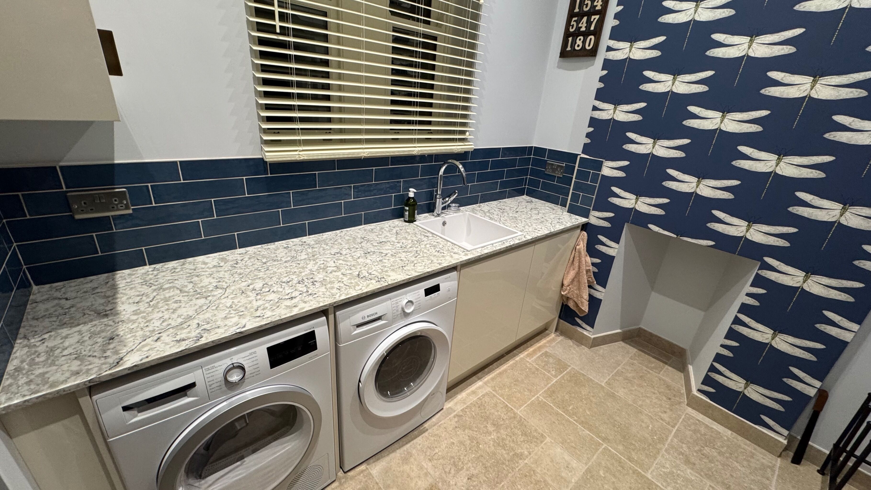 A kitchen with a built-in washer and dryer, a sink, and a window with blinds.
