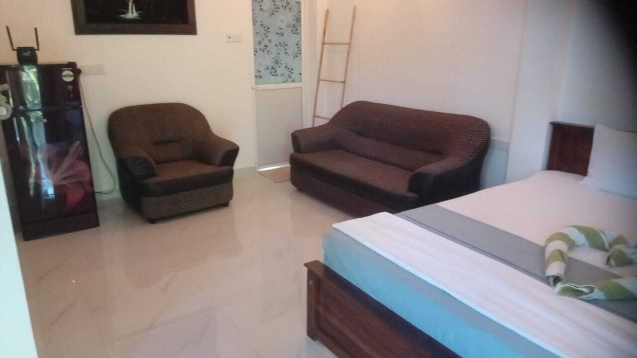 A bedroom with a bed, a brown armchair, a sofa, and a refrigerator.