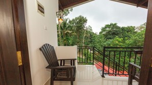 Ein Balkon mit einem Holzstuhl, einer weißen Wand und Blick auf üppiges Grün.