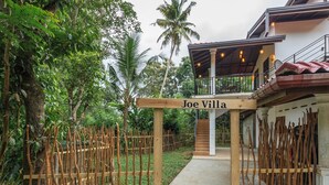 Ein hölzernes Tor mit der Aufschrift "Joe Villa" führt zu einem Haus mit überdachter Veranda und einer Treppe.