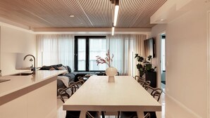 A modern kitchen with a central island, a dining area with a long table, and a living space with a sofa and a TV.