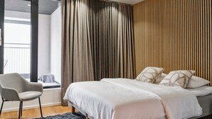 A modern bedroom with a large bed, a chair, and a window with curtains.
