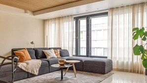 A modern living room with a grey sectional sofa, a round coffee table, and a large window with sheer curtains.