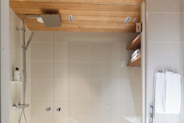 A modern shower area with a wooden ceiling, tiled walls, and a towel rack with towels. - Luxurious 3-Br Apt with Balcony (Helsinki)
