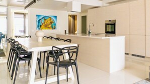 A modern kitchen with a central island, a dining area with chairs, and a large painting on the wall.