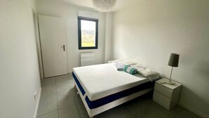 Ein Schlafzimmer mit Bett, Nachttisch, Lampe und Fenster.