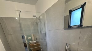 Ein modernes Badezimmer mit einer gläsernen Dusche, einem Holzwaschtisch mit weißem Waschbecken und einem Spiegel darüber.