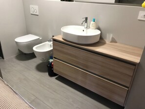 A modern bathroom with a white sink, a bidet, and a wooden vanity with drawers.