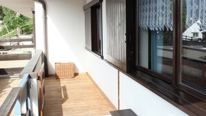 A wooden deck with a wicker basket, a sliding glass door with a lace curtain, and a white wall. - Suite Marco Nice Apartment in Cavalese With View (Cavalese)