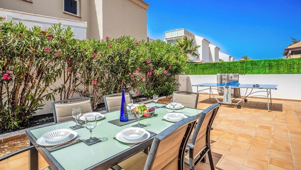 Patio esterno con tavolo apparecchiato per mangiare, circondato da piante e un cielo azzurro intenso.