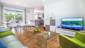 Un soggiorno moderno con tavolino in vetro, divano, televisore e zona pranzo con sedie e tavolo.