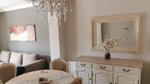 A dining area with a round table, chairs, a chandelier, a sofa, and a cabinet with a mirror.