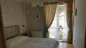 A bedroom with a bed, a radiator, a nightstand, and a window with curtains.