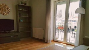 A hotel room with a large window, a sofa, a TV, and a bookshelf.