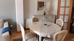 A dining area with a round table, white chairs, a chandelier, a mirror, and a cabinet.