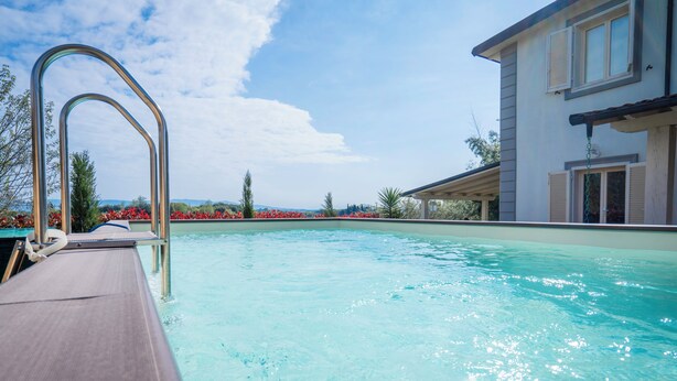 A swimming pool with a wooden deck and metal railings, surrounded by a building with large windows and a covered patio area. - Borgo House In Florentine Hills With Pool (Fucecchio)