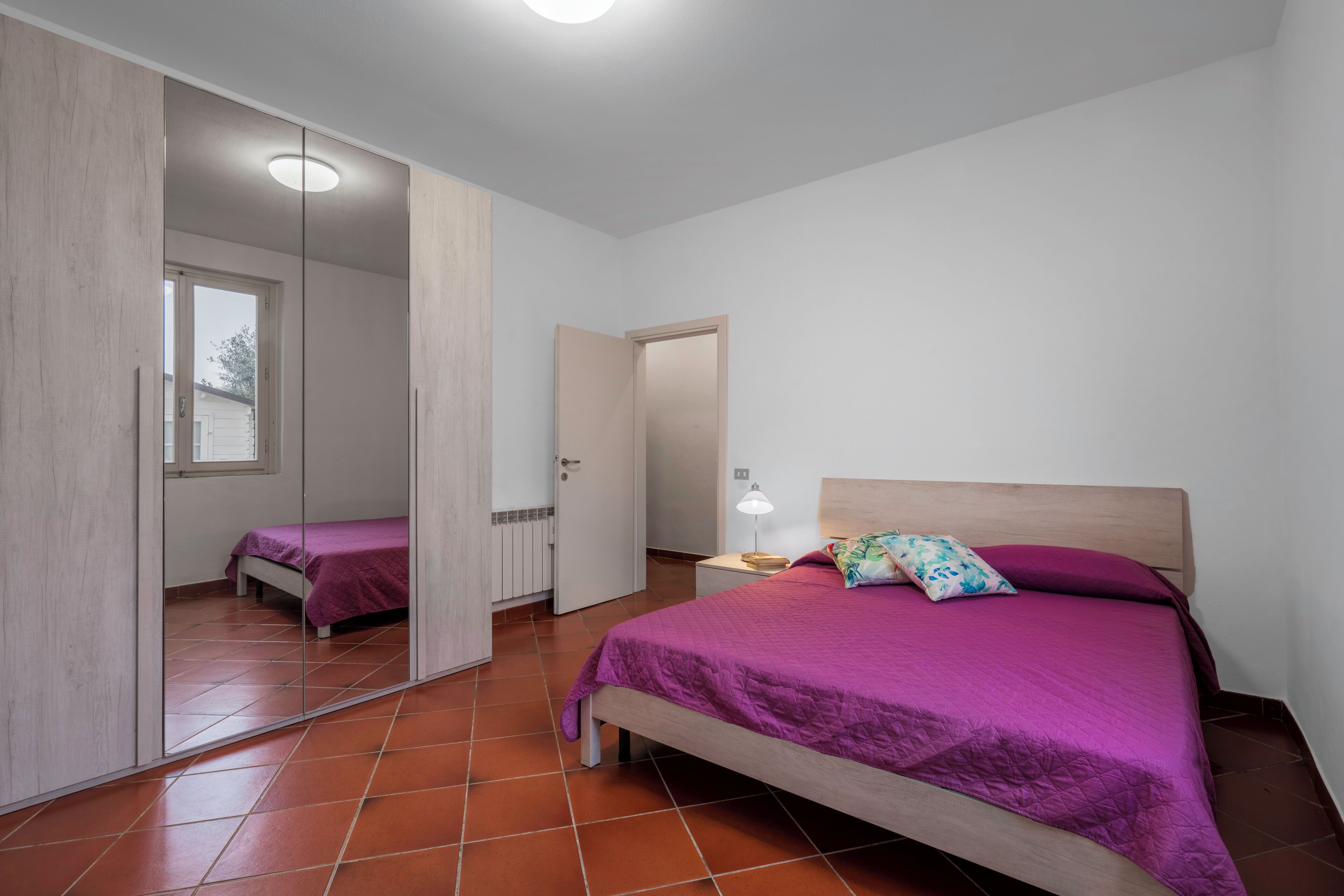 Ein Schlafzimmer mit Bett, Nachttisch, Spiegel und einer Tür zu einem anderen Raum.