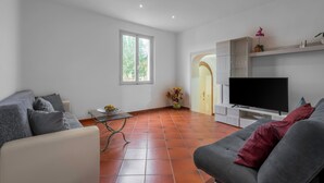 A living room with a grey sofa, a white armchair, a flat-screen TV, and a tiled floor. - Borgo House In Florentine Hills With Pool (Fucecchio)