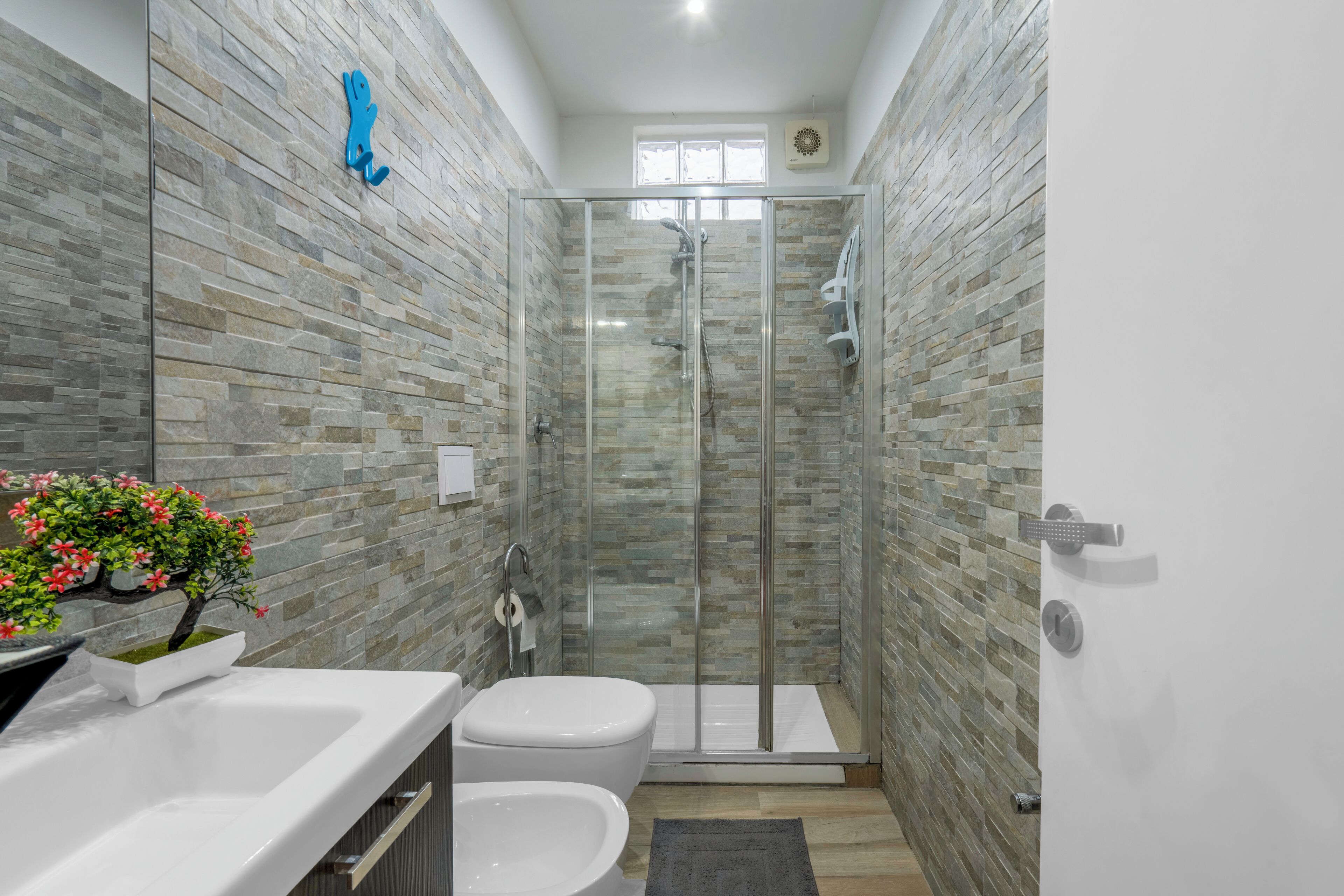 A modern bathroom with a glass-enclosed shower, a white sink, and a toilet.