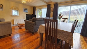 Una sala de estar acogedora con un sofá, una mesa de comedor con sillas, un televisor y una ventana con cortinas.
