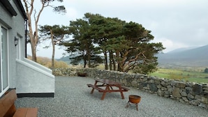 Un patio con muro de piedra, banca de madera, mesa de picnic y fogón.
